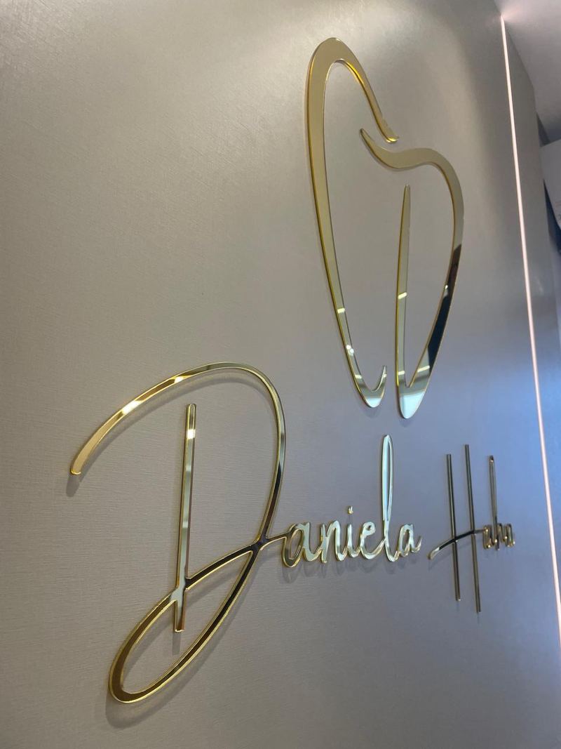 Nome e símbolo em acrílico dourado espelhado aplicados na parede de uma recepção